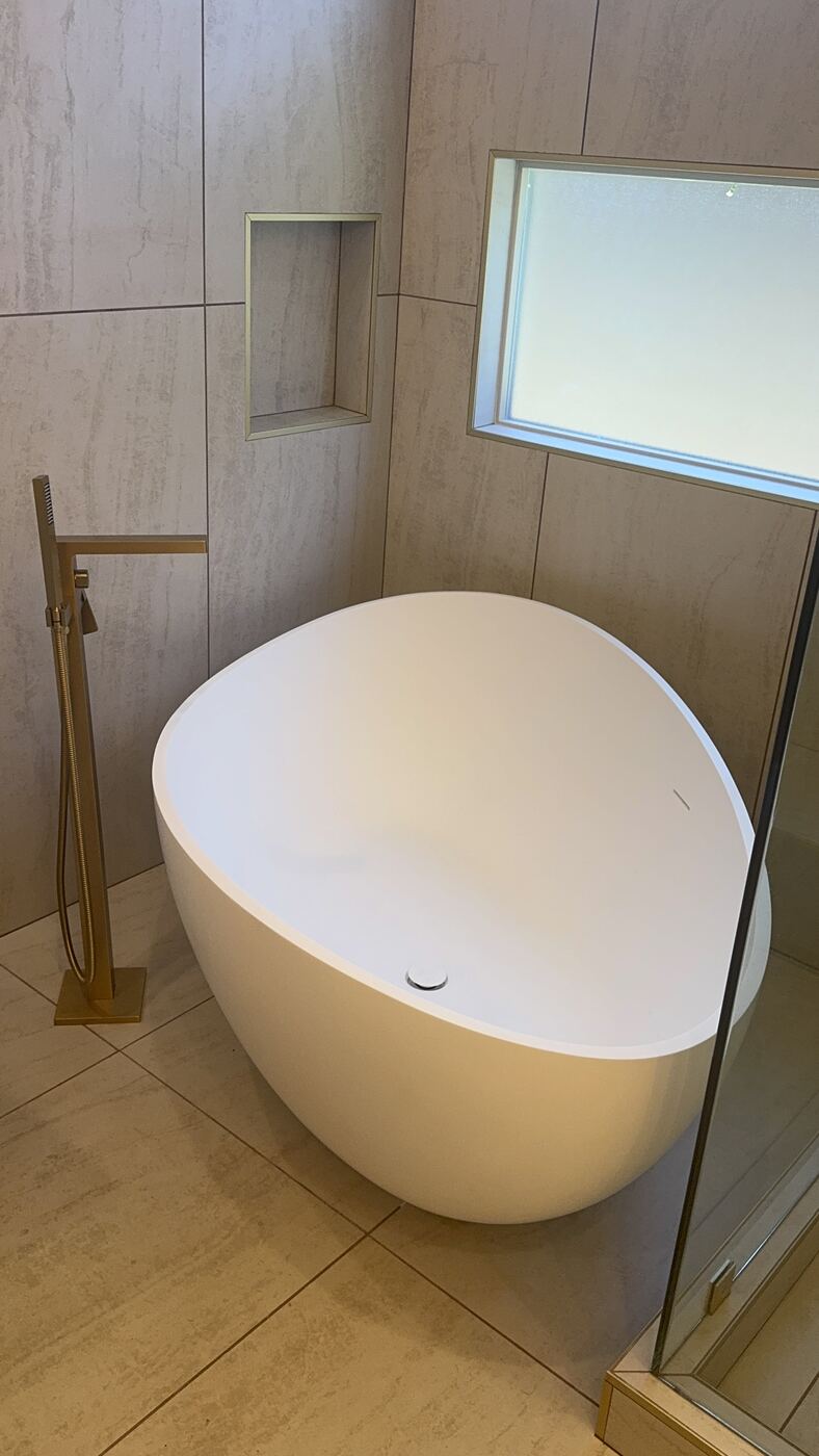 Freestanding white soaking tub with brushed gold floor-mount tub filler in a Las Vegas primary bath remodel