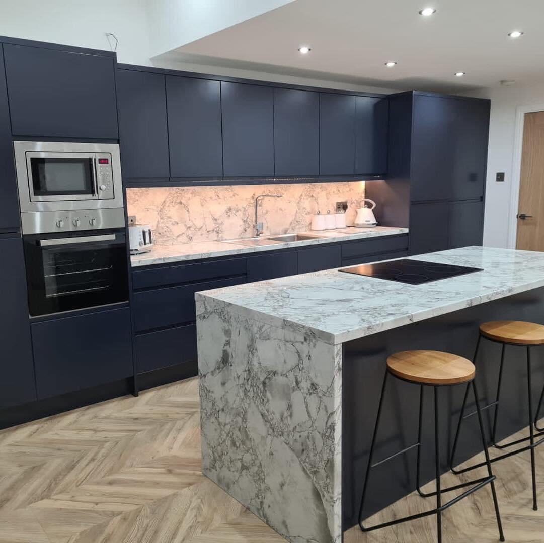 Modern kitchen renovation with navy blue cabinetry and marble waterfall island