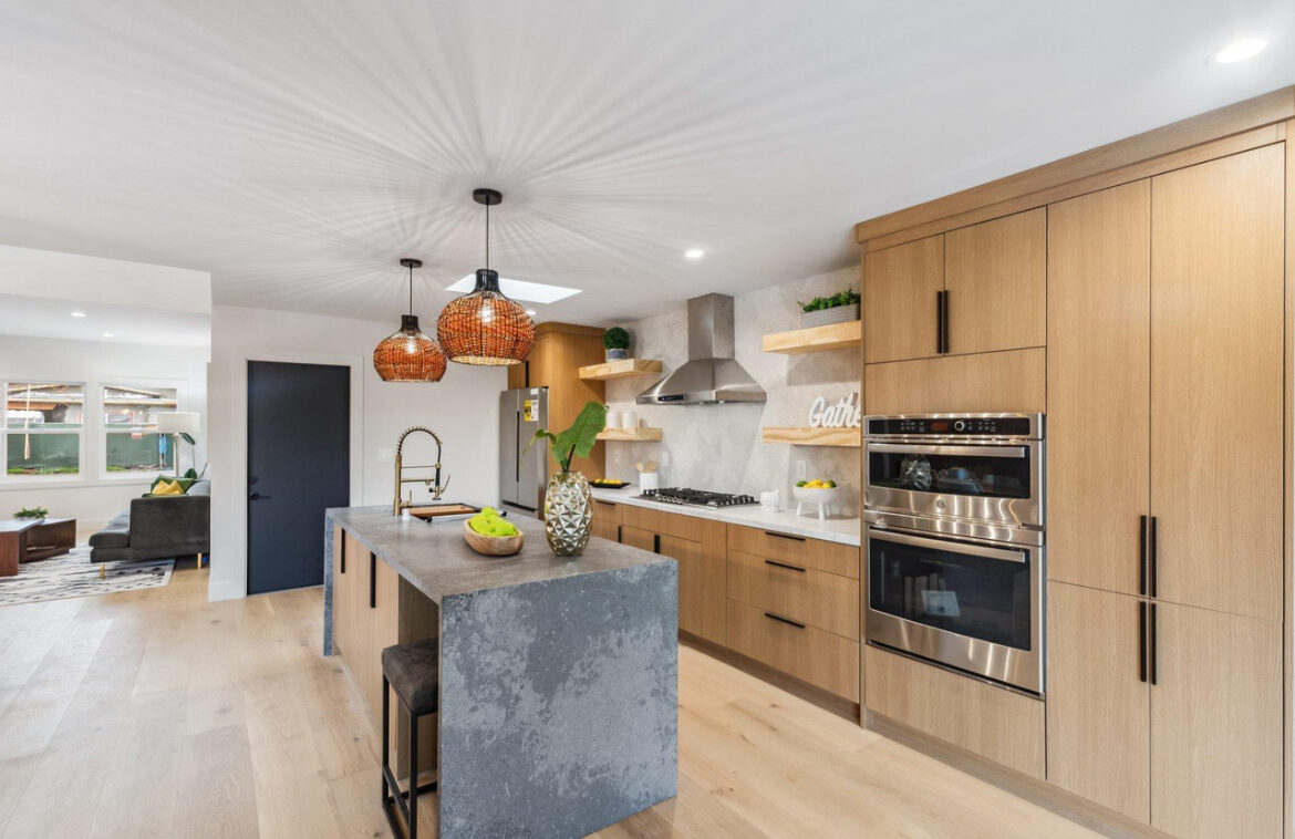 Open-concept kitchen renovation with wood cabinetry, black waterfall island and rattan pendants